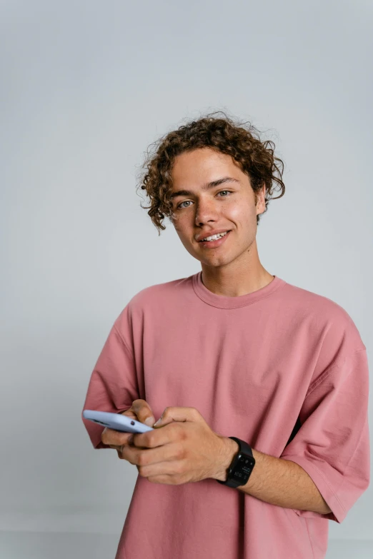 a man in a pink shirt holding a cell phone, a character portrait, trending on pexels, he has short curly brown hair, teenagers, high quality photo, skin : tjalf sparnaay