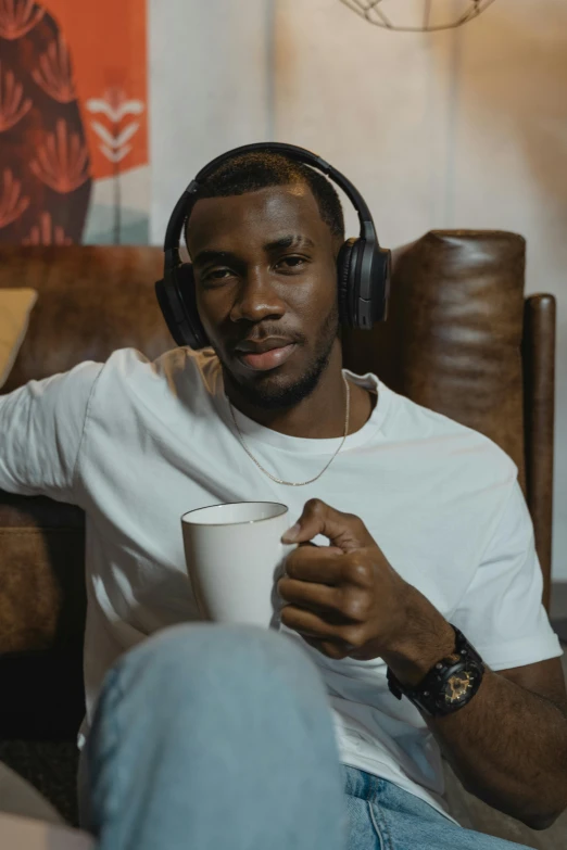 a man sitting on a couch with headphones on, trending on pexels, realism, with a cup of hot chocolate, man is with black skin, ( ( theatrical ) ), lgbtq