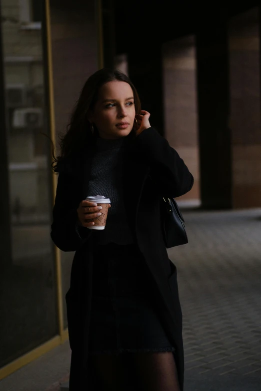 a woman talking on a cell phone while holding a cup of coffee, by Sven Erixson, pexels contest winner, realism, worn black coat, portrait sophie mudd, walking to work, ( ( theatrical ) )