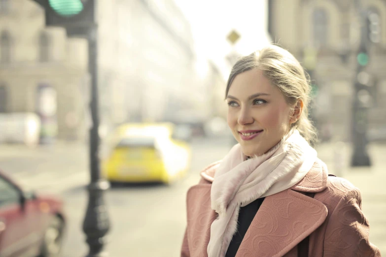 a woman standing on a city street next to a traffic light, by Mathias Kollros, pexels contest winner, warm and gentle smile, pink, scarf, avatar image