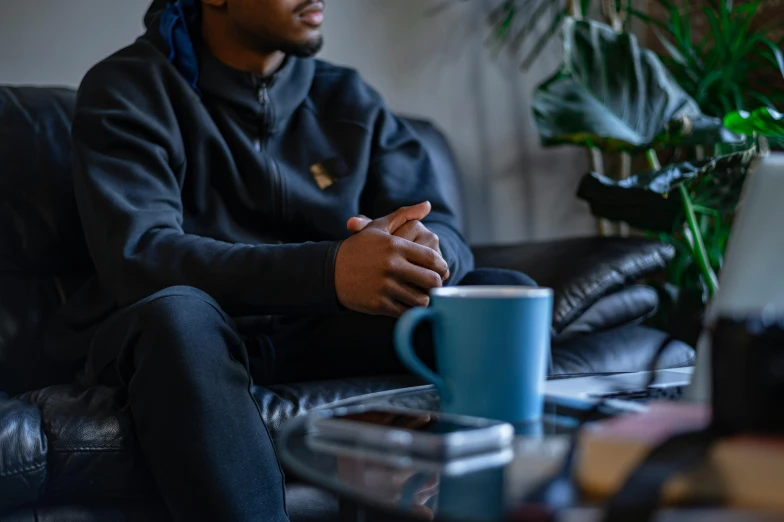 a man sitting on a couch next to a coffee cup, trending on pexels, wearing a tracksuit, black teenage boy, mental health, dark teal couch