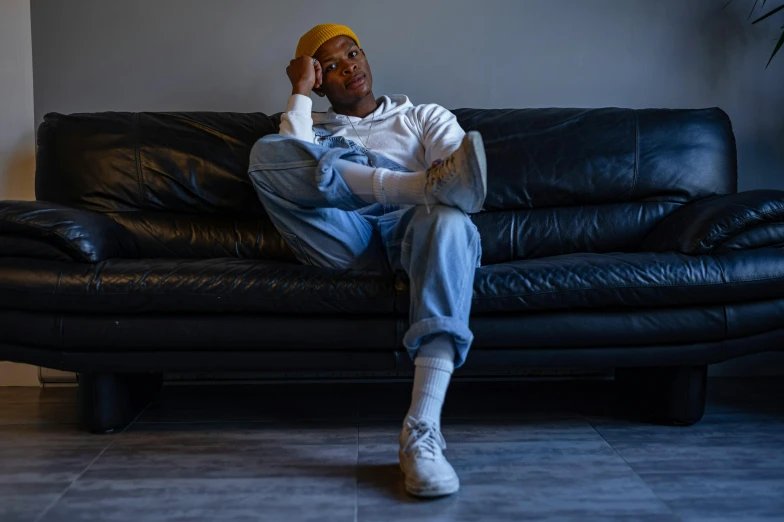 a man sitting on top of a black leather couch, trending on pexels, hyperrealism, tyler the creator, confident relaxed pose, wearing white sneakers, cinematic outfit photo