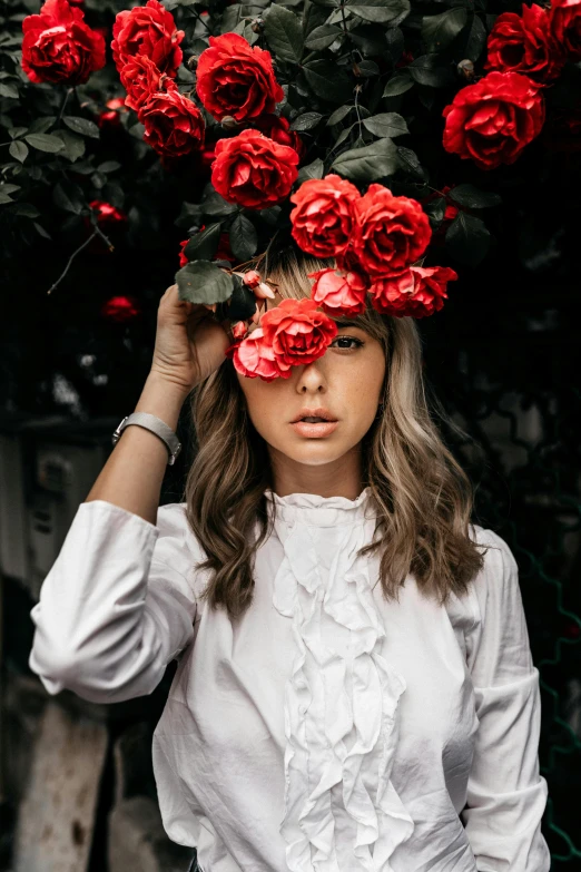 a woman standing in front of a bunch of red roses, a black and white photo, by Julia Pishtar, trending on unsplash, wearing a white button up shirt, halo over her head, sydney sweeney, clothes made out of flower