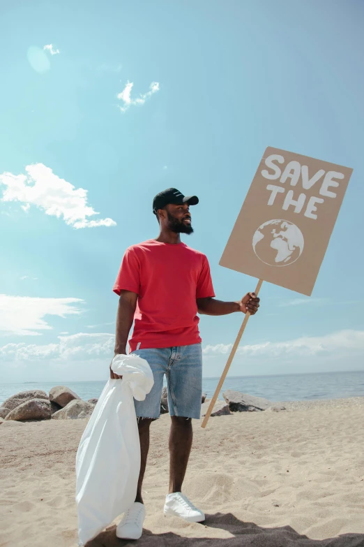 a man standing on a beach holding a sign, pexels contest winner, renaissance, sustainable materials, black man, garbage, mario