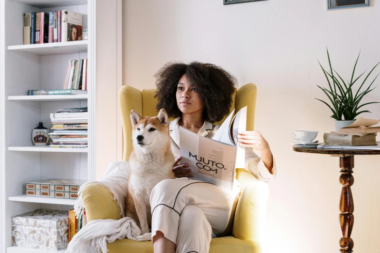 a woman sitting in a chair with a dog, by Julia Pishtar, pexels contest winner, with afro, reading nook, shibu inu, nathalie emmanuel