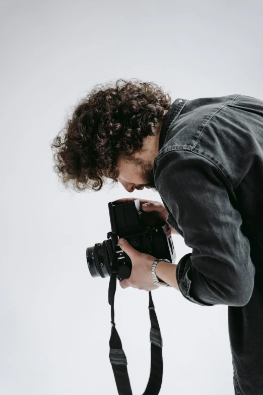 a man taking a picture with a camera, looking down on the camera, in front of white back drop, in an action pose, a photo of a man