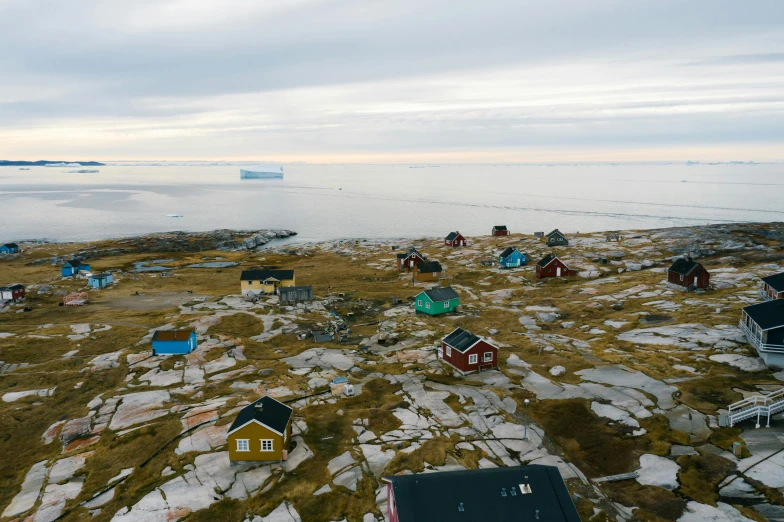 a group of houses sitting on top of a rocky hillside, by Dietmar Damerau, happening, icebergs in the background, drone view, multicoloured, inuk