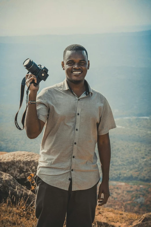 a man standing on top of a mountain holding a camera, osborne macharia, smiling male, professional photo-n 3, casual pose