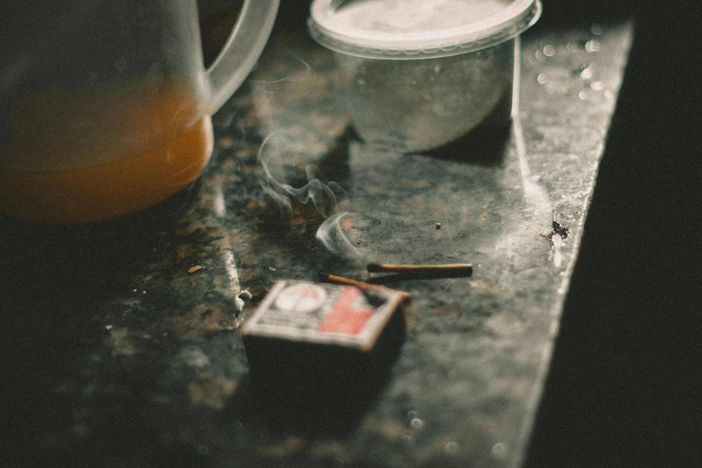 a cup sitting on top of a counter next to a cigarette, a still life, unsplash, process art, scratches and burns on film, drugs, chewing tobacco, oily substances