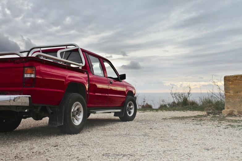 a red pickup truck parked on top of a dirt road, near the sea, high res photograph, profile, soft top