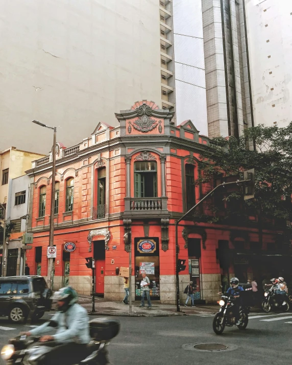 a group of motorcycles driving down a street next to tall buildings, by Matteo Pérez, pexels contest winner, art nouveau, red building, sao paulo, a multidimensional cozy tavern, old library