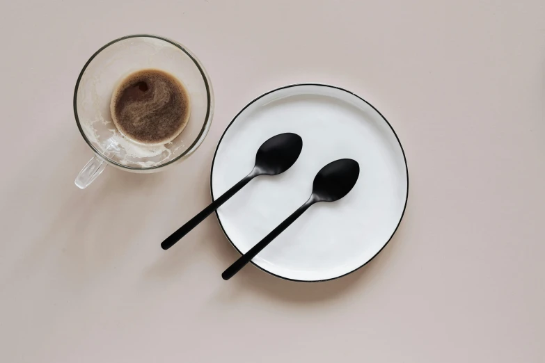 a white plate topped with two black spoons next to a cup of coffee, inspired by Peter de Sève, minimalism, black matte finish, various posed, enamel, soft oval face