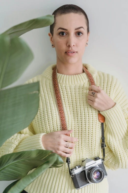 a woman in a yellow sweater holding a camera, inspired by Bernat Sanjuan, leather straps, neck zoomed in, sustainable materials, pastel'