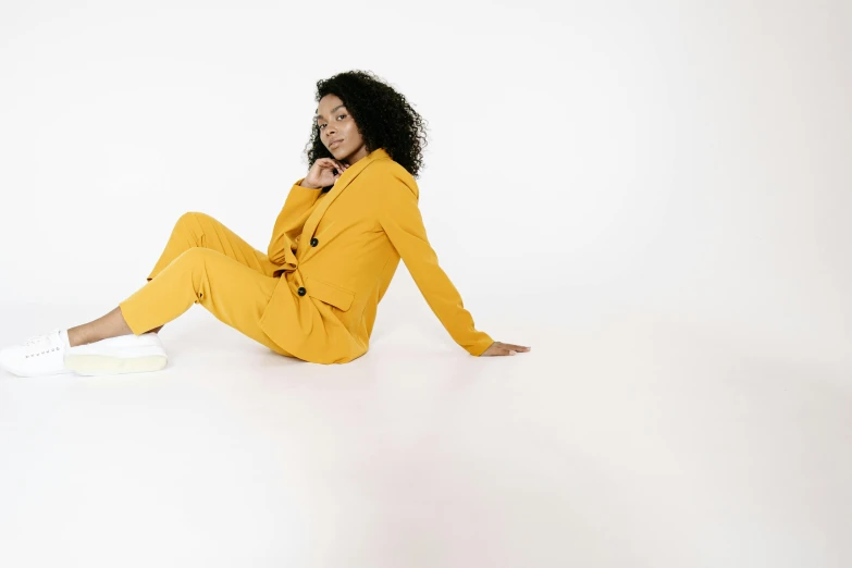 a woman in a yellow suit sitting on the floor, trending on pexels, antipodeans, in front of white back drop, tailored clothing, laying down, ashteroth