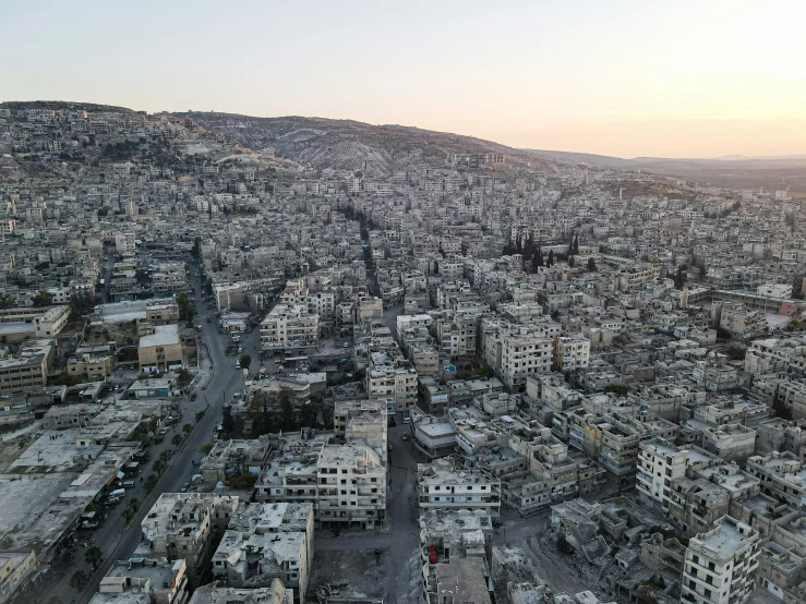 an aerial view of a city at sunset, hurufiyya, real life photo of a syrian man, white pale concrete city, unsplash photography, outdoors ruined cityscape