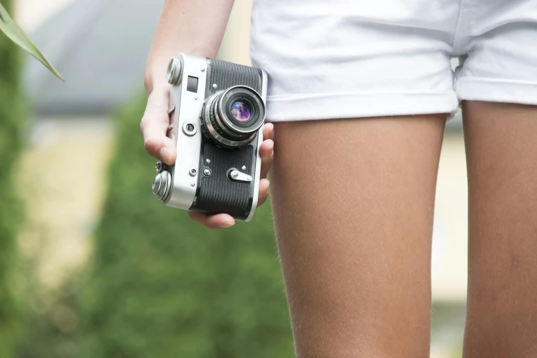 a close up of a person holding a camera, a picture, skimpy shorts, leica iii, miniskirt, wide - angle film