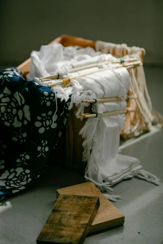 a basket sitting on top of a counter next to a cutting board, a silk screen, inspired by Shunbaisai Hokuei, unsplash, process art, spirits covered in drapery, ripped up white garment, installation, dark blue and white robes