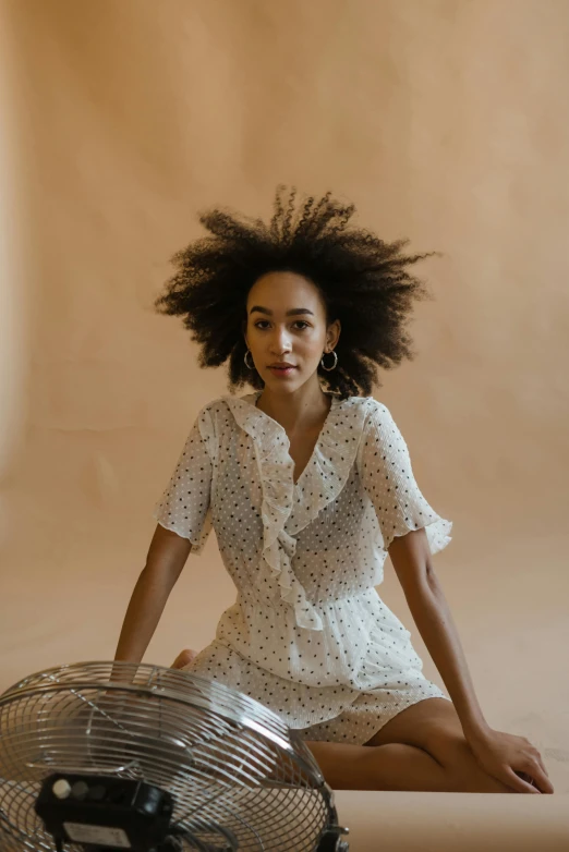 a woman sitting on the ground next to a fan, a portrait, trending on pexels, ashteroth, wearing a cute white dress, in a white boho style studio, patterned clothing