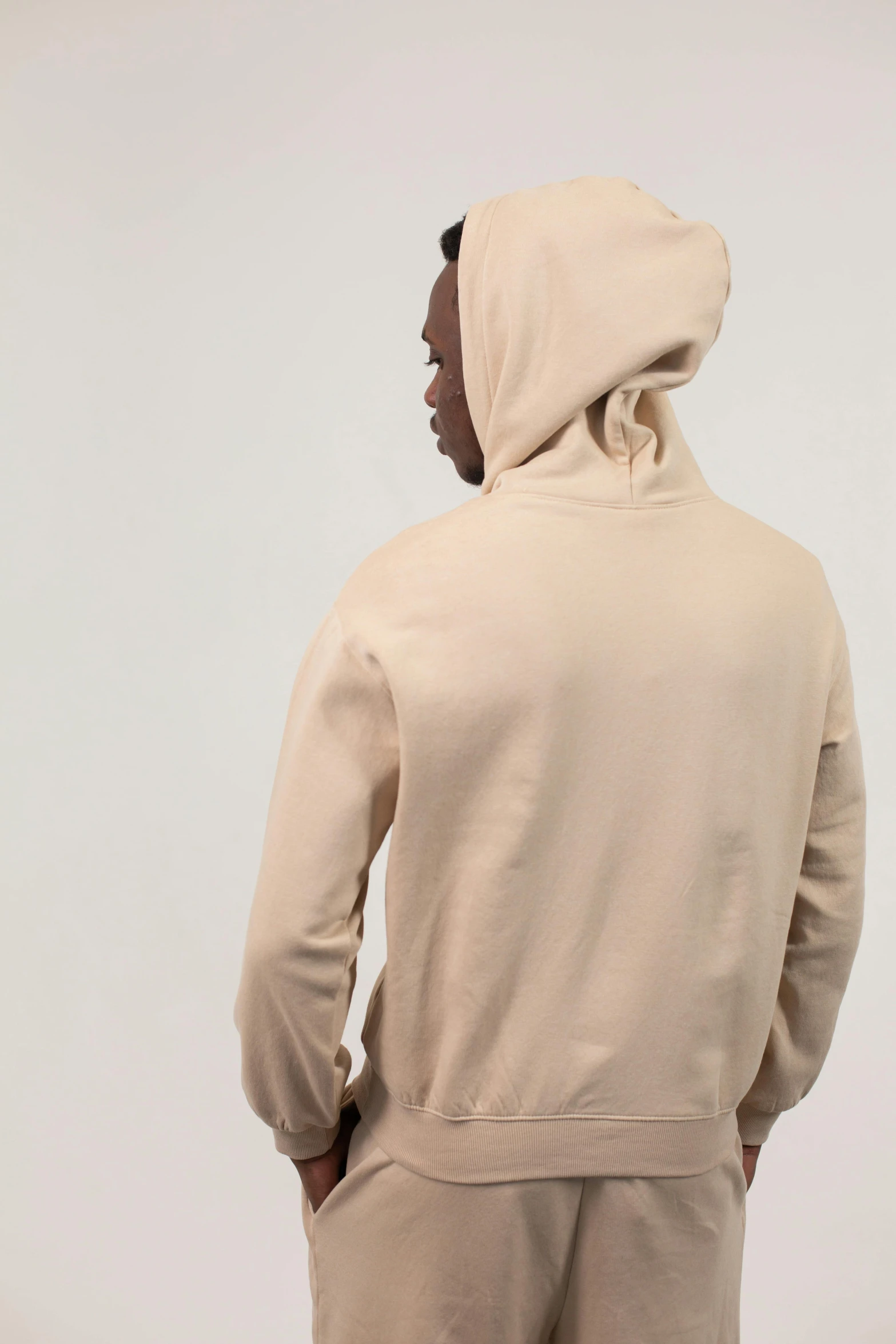 a man standing with his back to the camera, beige hoodie, full product shot, back view »