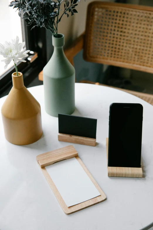 a cell phone sitting on top of a table next to a vase, a picture, product display, bamboo wood, chalk, display item