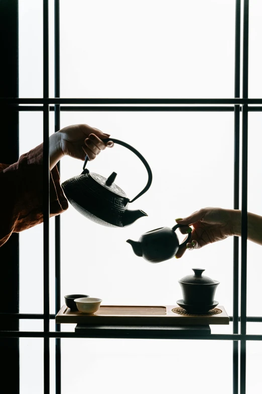 a person pouring tea into a cup in front of a window, inspired by Sesshū Tōyō, trending on unsplash, mingei, square, teapots, wearing black silk robes, reaching out to each other