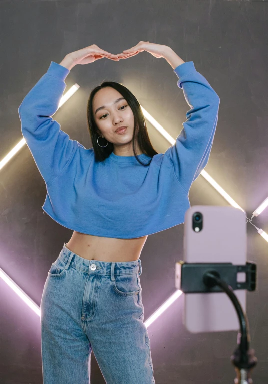 a woman standing in front of a camera, by Julia Pishtar, trending on pexels, holography, blue sweater, taking selfies, bare midriff, a young asian woman