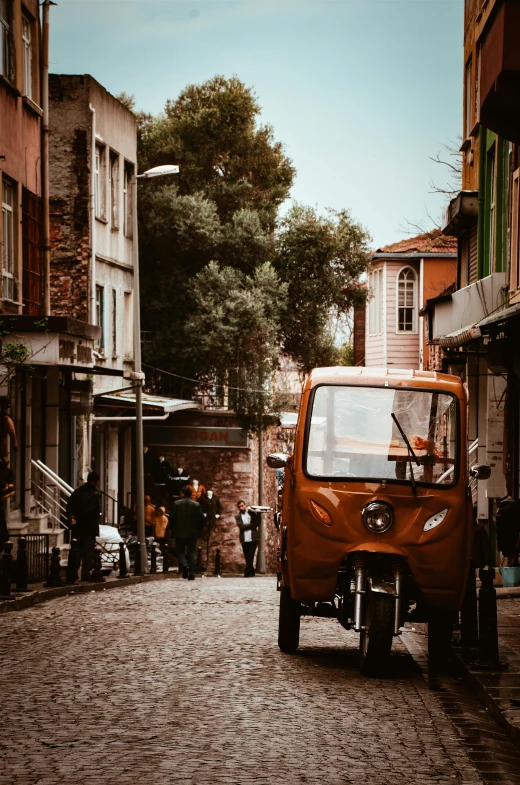 an orange truck driving down a cobblestone street, by Niyazi Selimoglu, pexels contest winner, fallout style istanbul, vintage photo, moped, brown