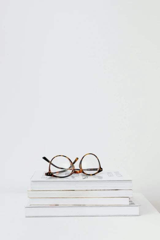 a pair of glasses sitting on top of a stack of books, by Nina Hamnett, minimalism, white with chocolate brown spots, white studio background, casually dressed, simple minimal