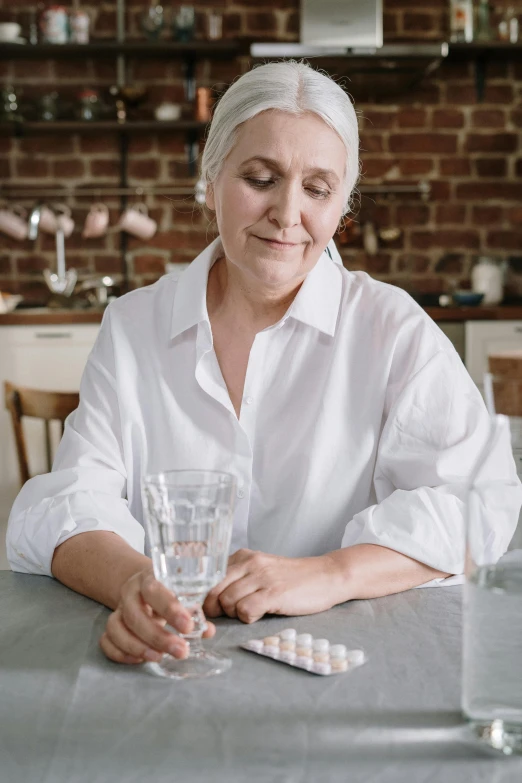 a woman sitting at a table with a glass of water, pills and medicine, white haired lady, upper body shot, profile image