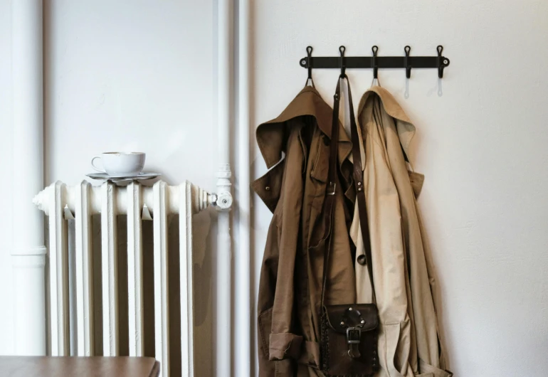 a coat rack hanging on a wall next to a radiator, inspired by August Sander, unsplash, trench coat, brown robes, 5 7 9, greatly detailed