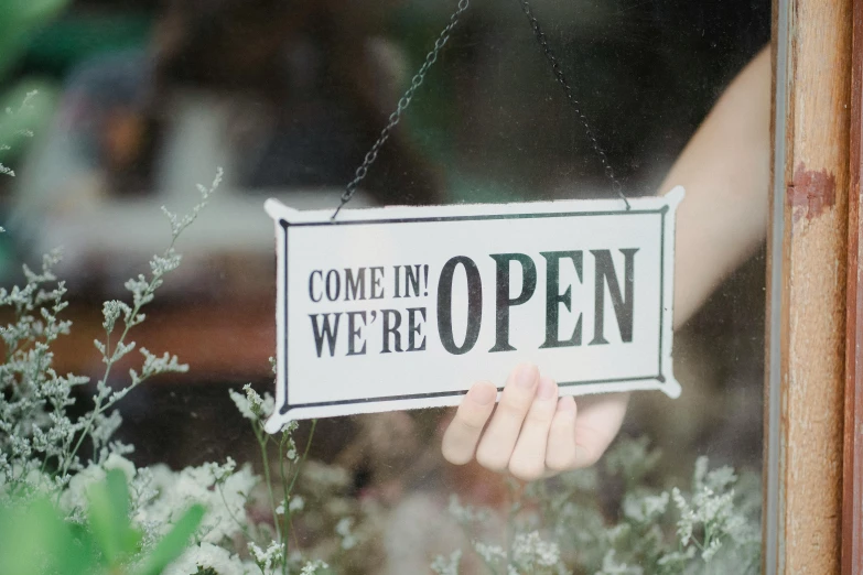 a person holding a sign that says come in we're open, pexels, happening, vinyl on glazing, lined in cotton, fine intricate, thumbnail