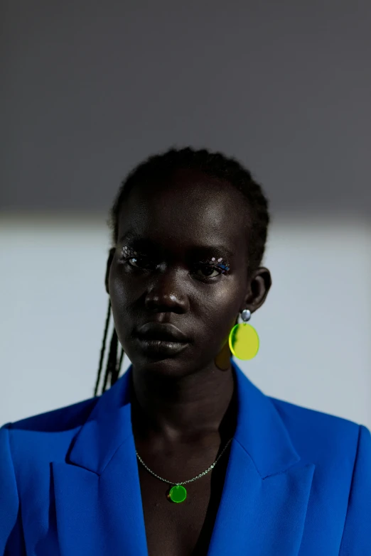 a woman in a blue jacket and yellow earrings, trending on unsplash, afrofuturism, brutalist fashion show, adut akech, hito steyerl, unmistakably kenyan