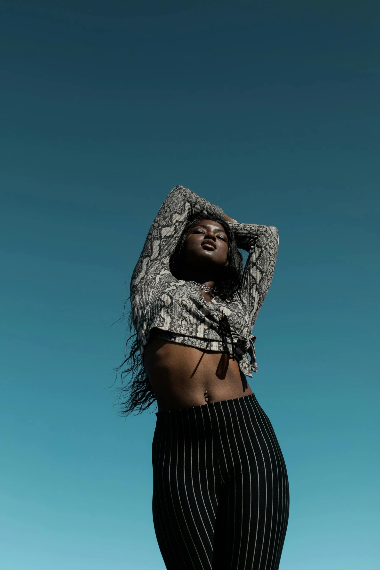 a woman standing in front of a blue sky, by Gavin Hamilton, trending on pexels, wearing a sexy cropped top, black skin!!!, patterned clothing, expressive pose