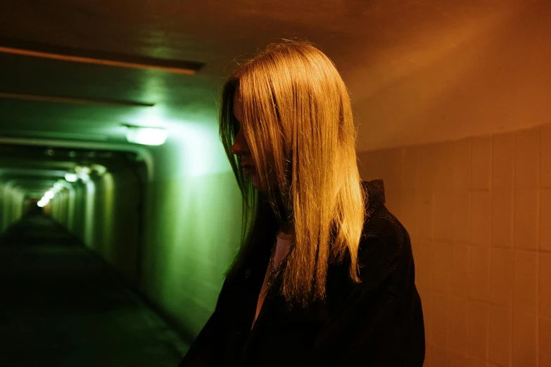 a woman with long blonde hair standing in a tunnel, inspired by Elsa Bleda, unsplash, realism, pale green glow, evening lighting, frank moth, woman in streetwear