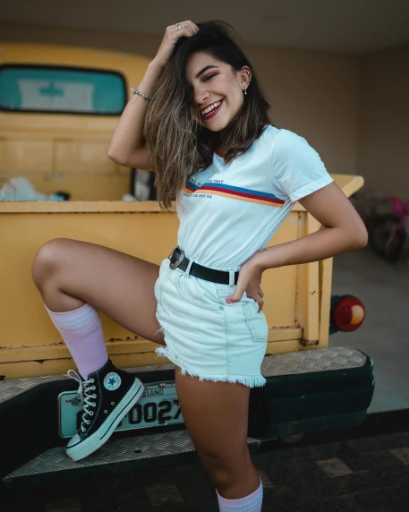 a woman posing in front of a yellow truck, inspired by Elsa Bleda, trending on pexels, wearing shorts and t shirt, rainbow accents, grinning lasciviously, girl wearing uniform