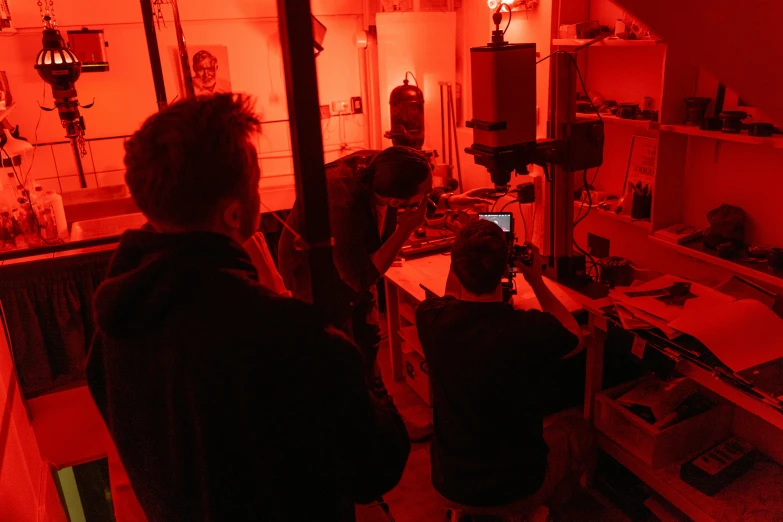 a couple of people that are standing in a room, darkroom, red orange lighting, gunsmithing, spooky lighting