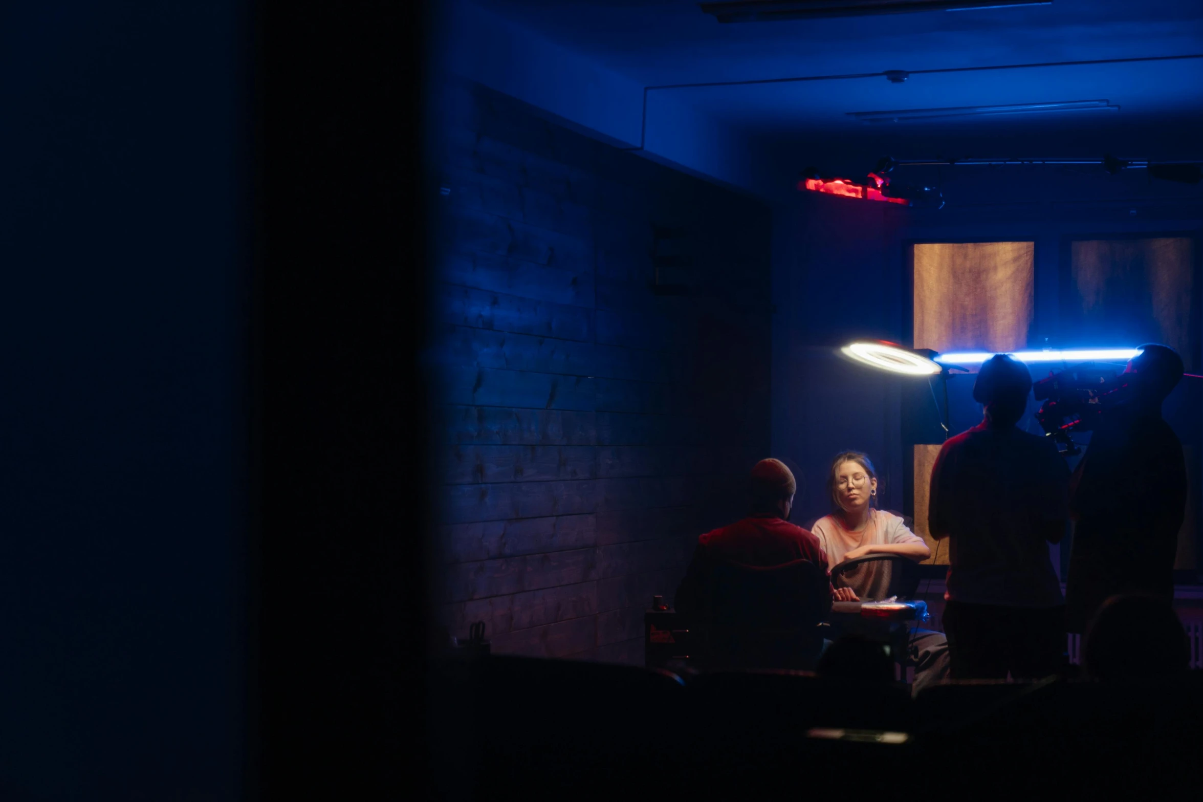 a group of people sitting around a table in a dark room, cinematatic lighting, blue and red lighting, minimalist cinematic lighting, inside a bar