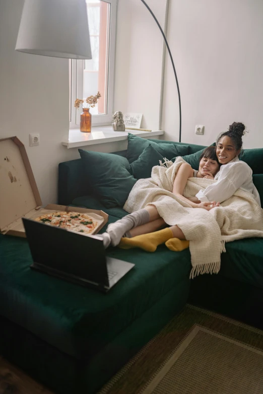 a woman laying on top of a green couch next to a laptop, a picture, trending on pexels, renaissance, hugging each other, sharing a pizza, netflix series, two people