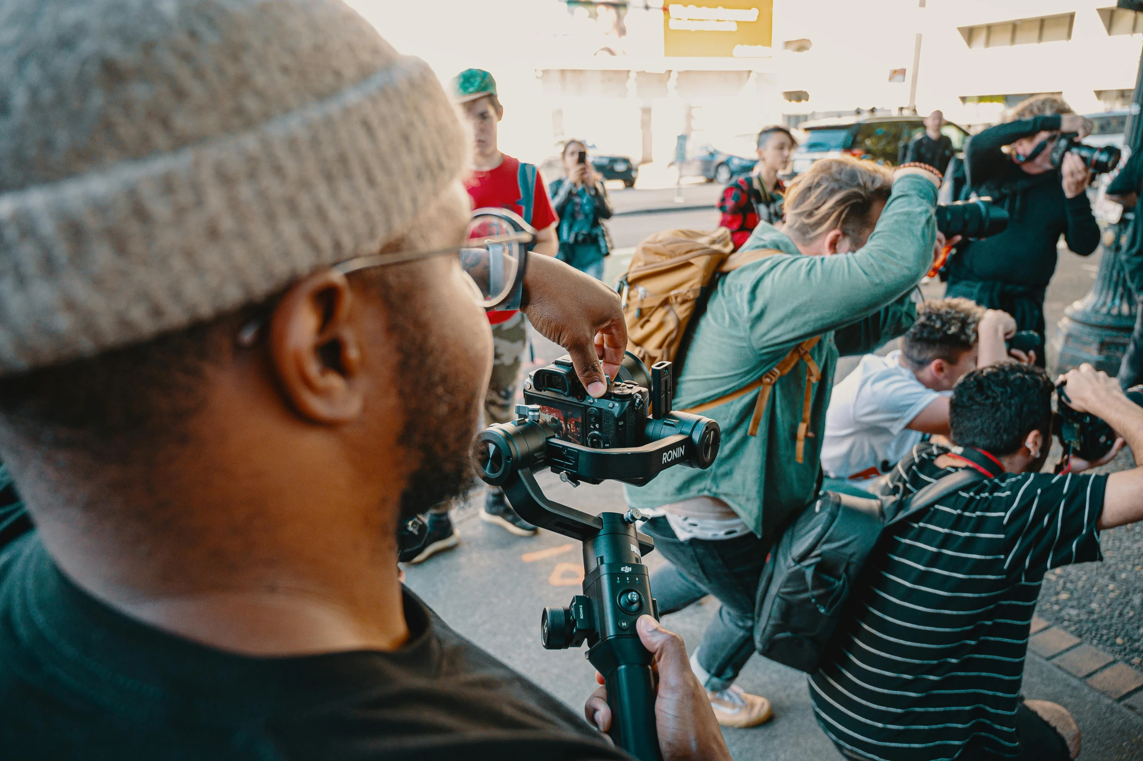 a man holding a camera in front of a crowd of people, anamorphic cinematography, instagram post, exterior shot, diverse