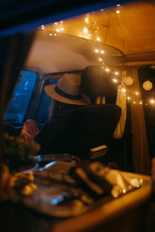 a man in a hat sitting in the back of a car, by Jessie Algie, unsplash contest winner, romanticism, fairy lights, van, glamping, fully decorated