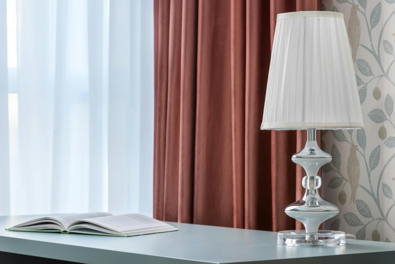 a lamp sitting on top of a table next to a book, curtains, hotel room, silver white red details, light academia aesthetic