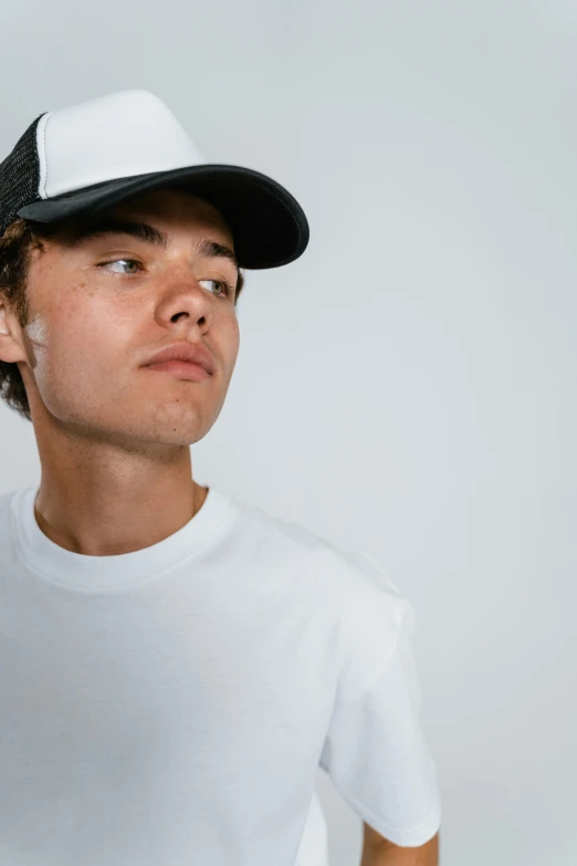 a young man wearing a white t - shirt and a black hat, trending on unsplash, plain background, wearing a baseball hat, orelsan, low quality photo