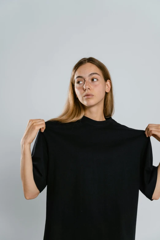 a woman holding up a black t - shirt, by Tobias Stimmer, neck wrinkles, thicc, long shirt, young woman in a dress