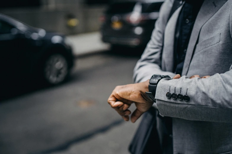 a man in a suit is looking at his watch, by Carey Morris, pexels contest winner, cars and people, grey clothes, holding arms on holsters, busy streets