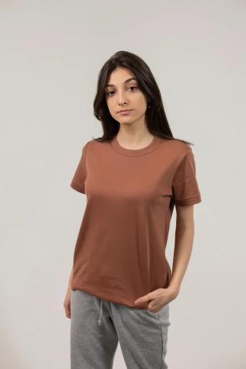 a woman standing with her hands in her pockets, pexels contest winner, hurufiyya, wearing an orange t-shirt, muted brown, high resolution product photo, made of bronze