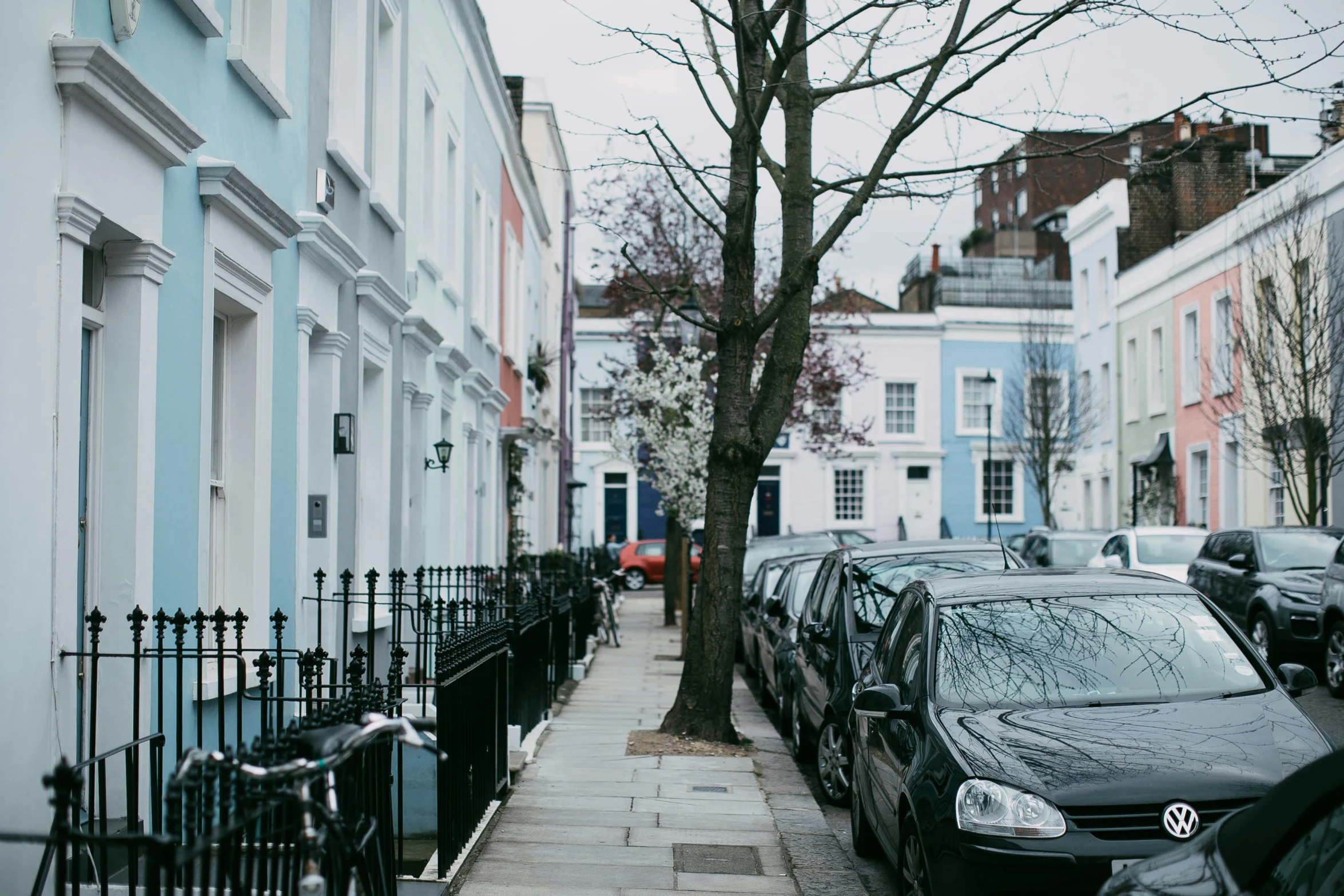 a row of parked cars on a city street, by Penelope Beaton, pexels contest winner, visual art, white houses, trees around, ignant, jane austen