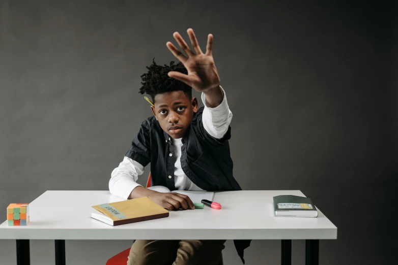 a man sitting at a desk with his hands in the air, trending on pexels, ashcan school, black teenage boy, angry looking at camera, high quality photo, sitting on top a table