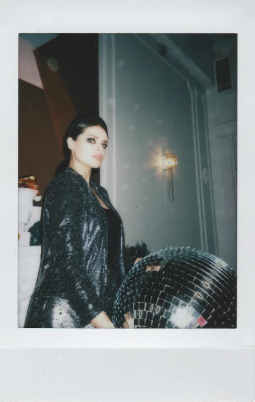 a woman standing in front of a disco ball, a polaroid photo, wearing a fancy black jacket, with straight black hair, violet myers, petra cortright