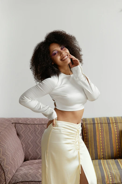 a woman standing in a living room next to a couch, trending on pexels, arabesque, white silky outfit, with afro, wearing crop top and miniskirt, satisfied pose