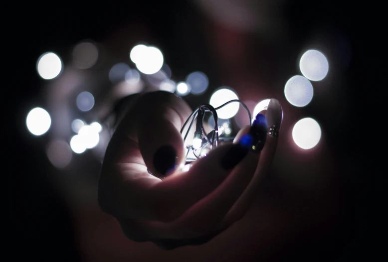 a person holding a string of lights in their hand, a macro photograph, by David Donaldson, unsplash, jewelled, dark and white, digital artwork, multiple stories